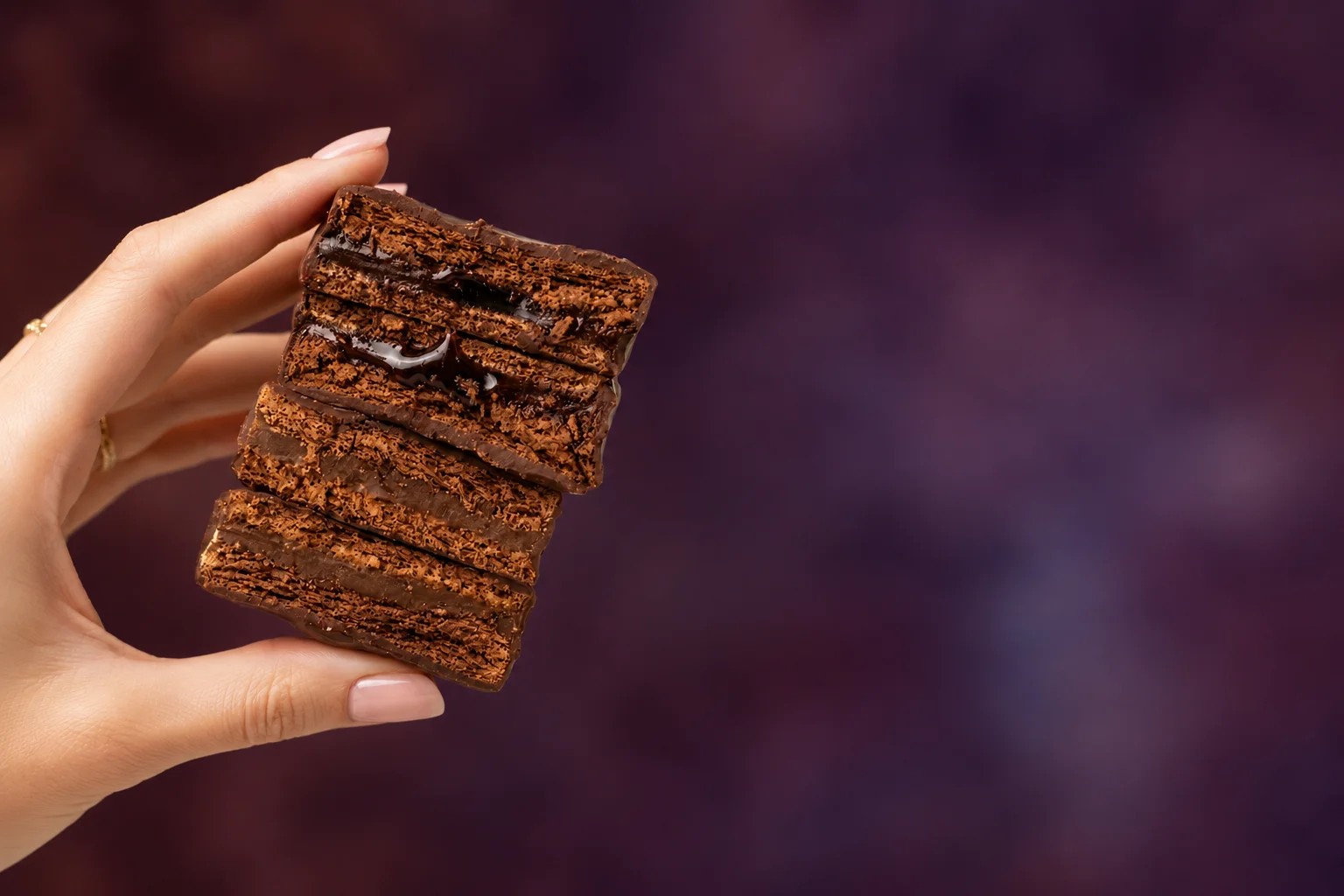 Mano sosteniendo un alfajor PETRA partido, mostrando las capas de chocolate y relleno